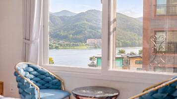 A room with a view of a lake and mountains, a blue chair, and a small round table.