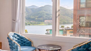 A room with a view of a lake and mountains, a blue chair, and a small round table.