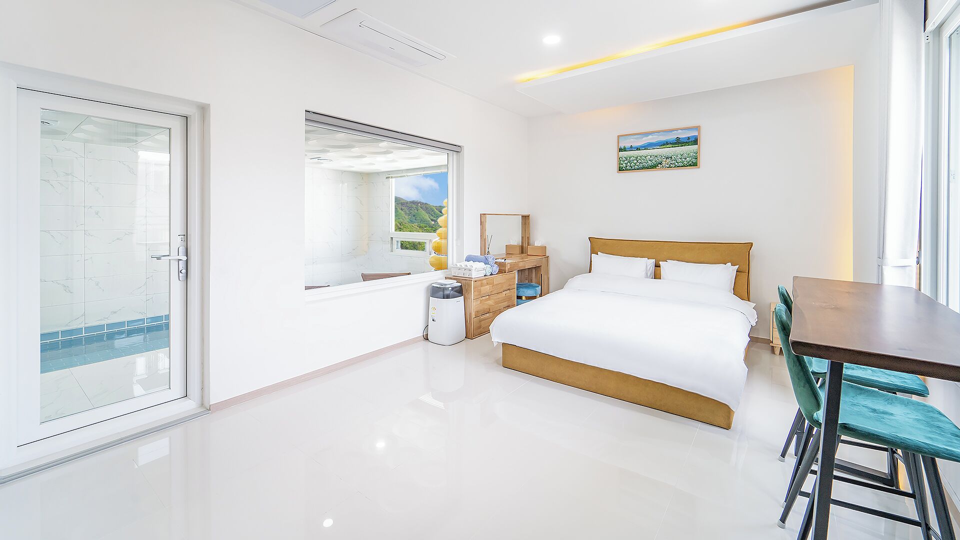 Un dormitorio moderno con cama, escritorio y vistas a un paisaje verde a través de una ventana.