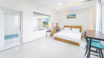 Un dormitorio moderno con cama, escritorio y vistas a un paisaje verde a través de una ventana.