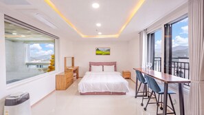 A modern bedroom with a bed, bedside tables, a desk with chairs, a large window, and a painting on the wall.