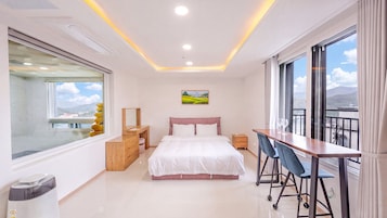 Un dormitorio moderno con cama, mesitas de noche, un escritorio con sillas, un ventanal grande y un cuadro en la pared.