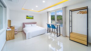 Une chambre d’hôtel moderne équipée d’un lit, d’un bureau avec des chaises, d’une armoire et d’une grande fenêtre donnant sur un paysage verdoyant.