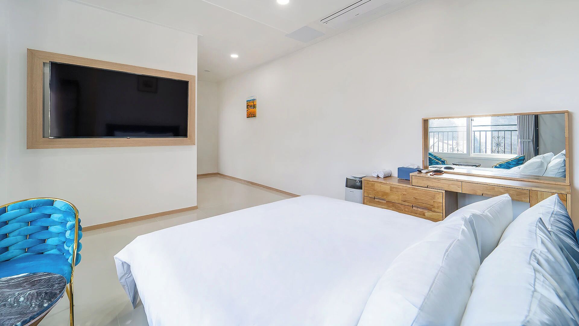 A hotel room with a bed, a desk with a mirror, a chair, and a TV mounted on the wall.