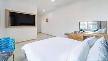 A hotel room with a bed, a desk with a mirror, a chair, and a TV mounted on the wall.