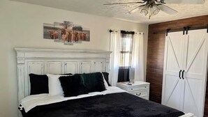 Une chambre à coucher avec un lit blanc, une literie noire et blanche, une table de chevet, une commode, un ventilateur de plafond et une armoire.