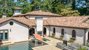 Zona de piscina con vista despejada, un área de estar cubierta y un edificio con techo de tejas y ventanas arqueadas.