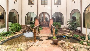 Un patio con un puente de piedra, un estanque pequeño y plantas en macetas.