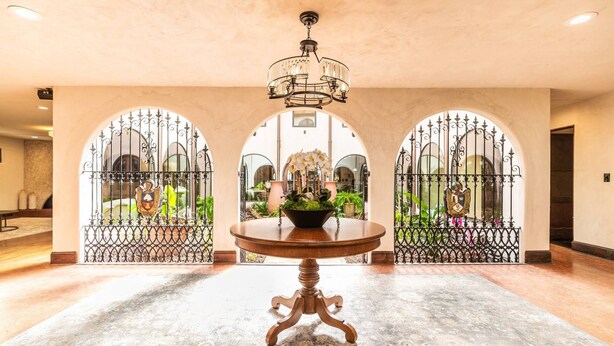 Un vestíbulo con una mesa redonda de madera, un candelabro y tres arcos con puertas de hierro decorativas.