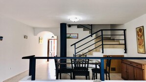A dining area with a glass table and chairs, a staircase with a black railing, and a painting on the wall. - Incredible duplex in La Lajita (La Lajita)