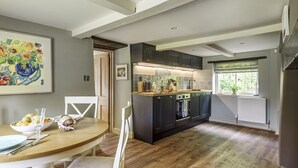 Une cuisine moderne avec des meubles de couleur sombre, une table à manger en bois et un grand tableau accroché au mur.