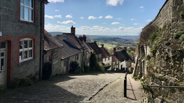 Une ruelle étroite pavée, bordée de bâtiments anciens en pierre, dotés de toits à pignons traditionnels et de cheminées apparentes.