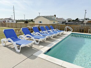 A swimming pool with blue lounge chairs and a wooden deck.