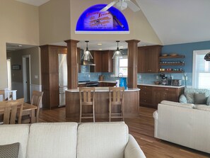 Une cuisine moderne avec des meubles en bois, un îlot central doté de tabourets, et un coin repas avec une table et des chaises.