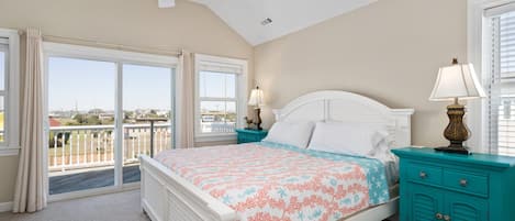 A bedroom with a bed, two nightstands, a ceiling fan, and a view through large windows.
