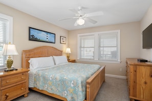 A bedroom with a bed, wooden nightstands, a ceiling fan, and a television. - Turning Tide: Semi-Oceanfront, private pool & hot tub, rec room with pool table! (Nags Head)