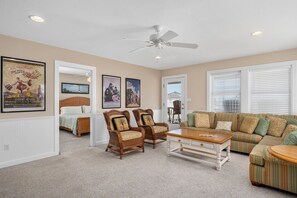 A spacious living room with a large sofa, two wicker chairs, a coffee table, and a ceiling fan.