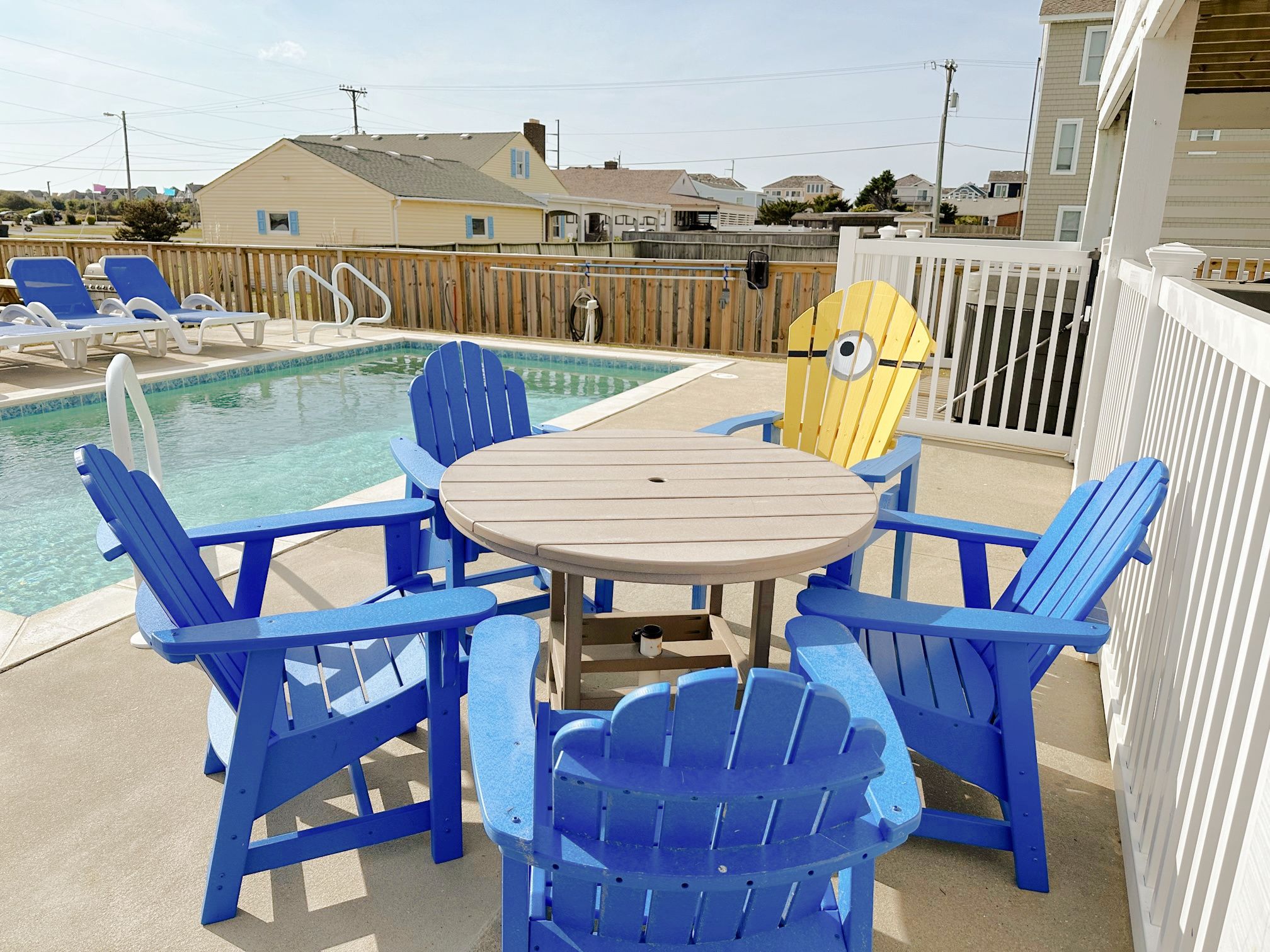 Un área junto a la piscina con sillas Adirondack azules y una mesa de madera.