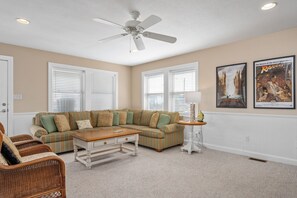 A living room with a sectional sofa, a coffee table, wicker chairs, a ceiling fan, and two framed movie posters.