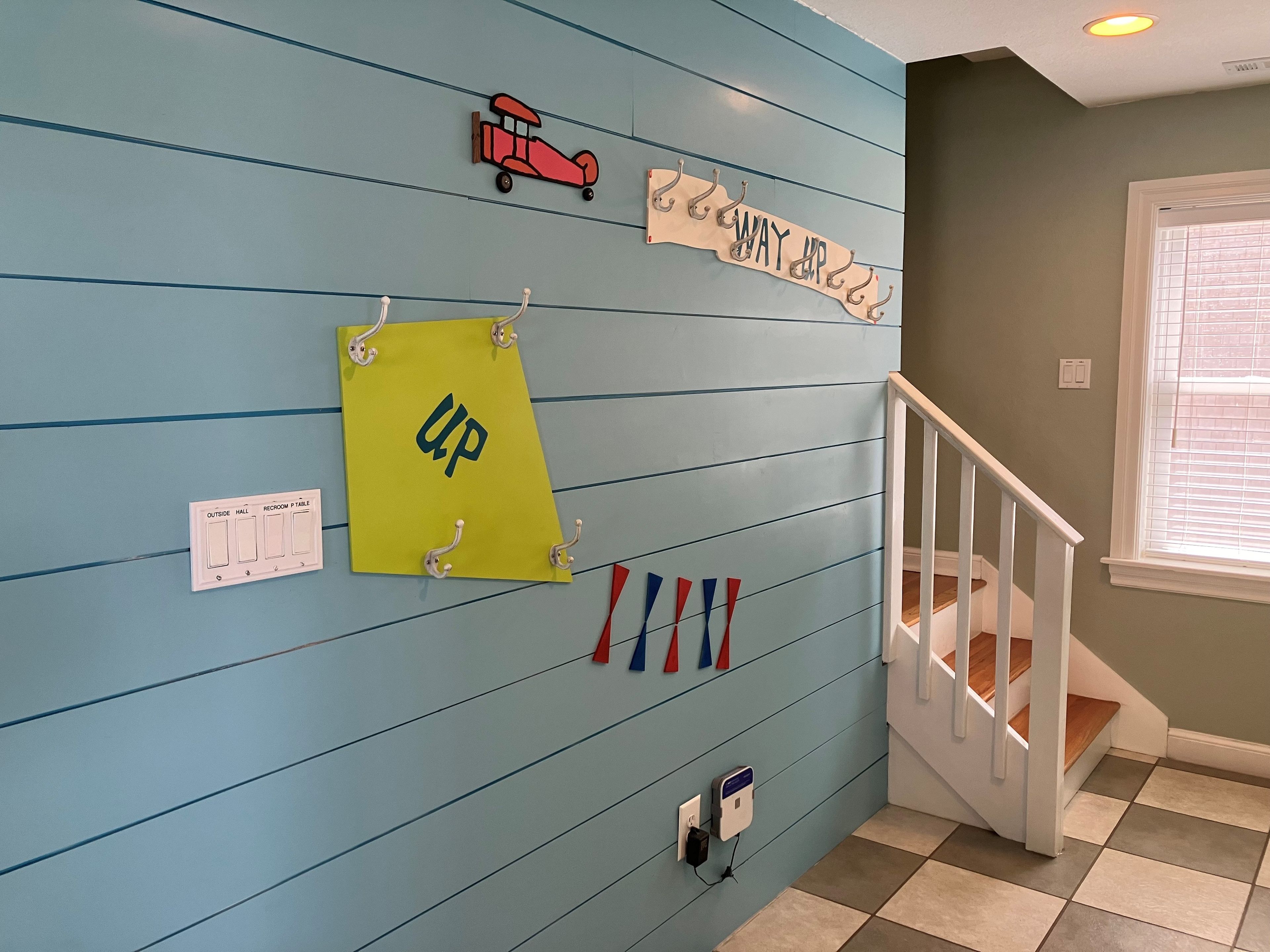 A hallway with a blue wall, a yellow sign with 'UP' written on it, a red toy car, a 'WAY UP' sign, and a set of red and blue flags.