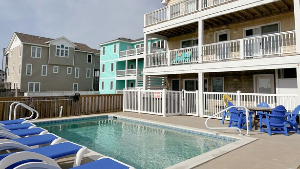 Un espace piscine avec des chaises longues et une terrasse entourée d’une clôture.