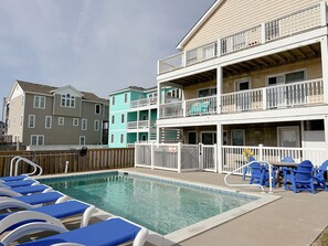 A pool area with lounge chairs and a fenced deck. - Turning Tide: Semi-Oceanfront, private pool & hot tub, rec room with pool table! (Nags Head)