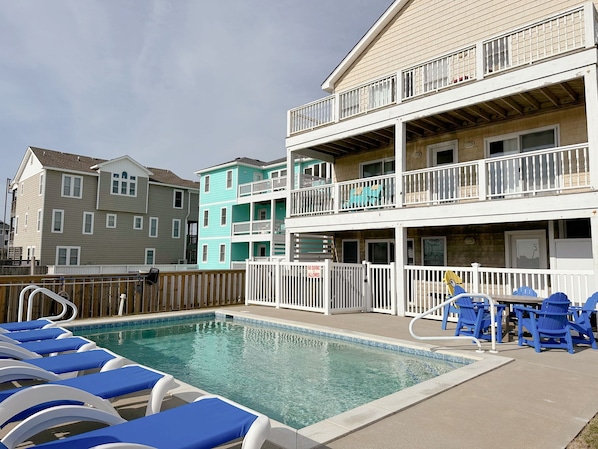 Un espace piscine avec des chaises longues et une terrasse entourée d’une clôture.