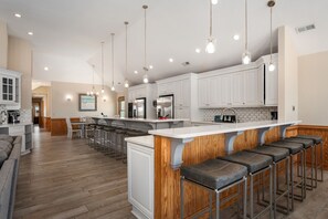 A modern kitchen with white cabinetry, a central island with bar stools, and pendant lighting. - Turtle's Nest: Oceanfront, pool, hot tub, theater & rec rooms and elevator! (Kill Devil Hills)