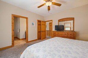 A bedroom with a bed, dresser, television, and a ceiling fan.