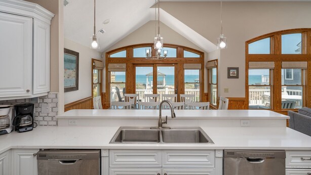 A kitchen with a large island, double sink, and wooden cabinets. There are large windows with a view of the ocean. - Turtle's Nest: Oceanfront, pool, hot tub, theater & rec rooms and elevator! (Kill Devil Hills)