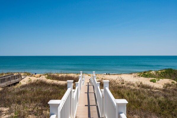 A wooden boardwalk leading to the beach with white railings and a clear view of the ocean.