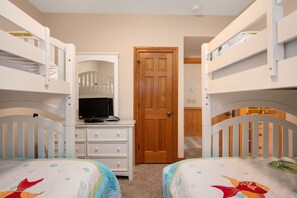 A bedroom with bunk beds, a wooden door, a dresser with drawers, and a television on the dresser. - Turtle's Nest: Oceanfront, pool, hot tub, theater & rec rooms and elevator! (Kill Devil Hills)