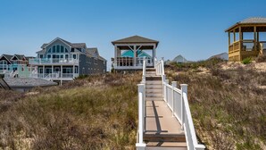 A wooden boardwalk leading to beach houses with large windows and a gazebo. - Turtle's Nest: Oceanfront, pool, hot tub, theater & rec rooms and elevator! (Kill Devil Hills)