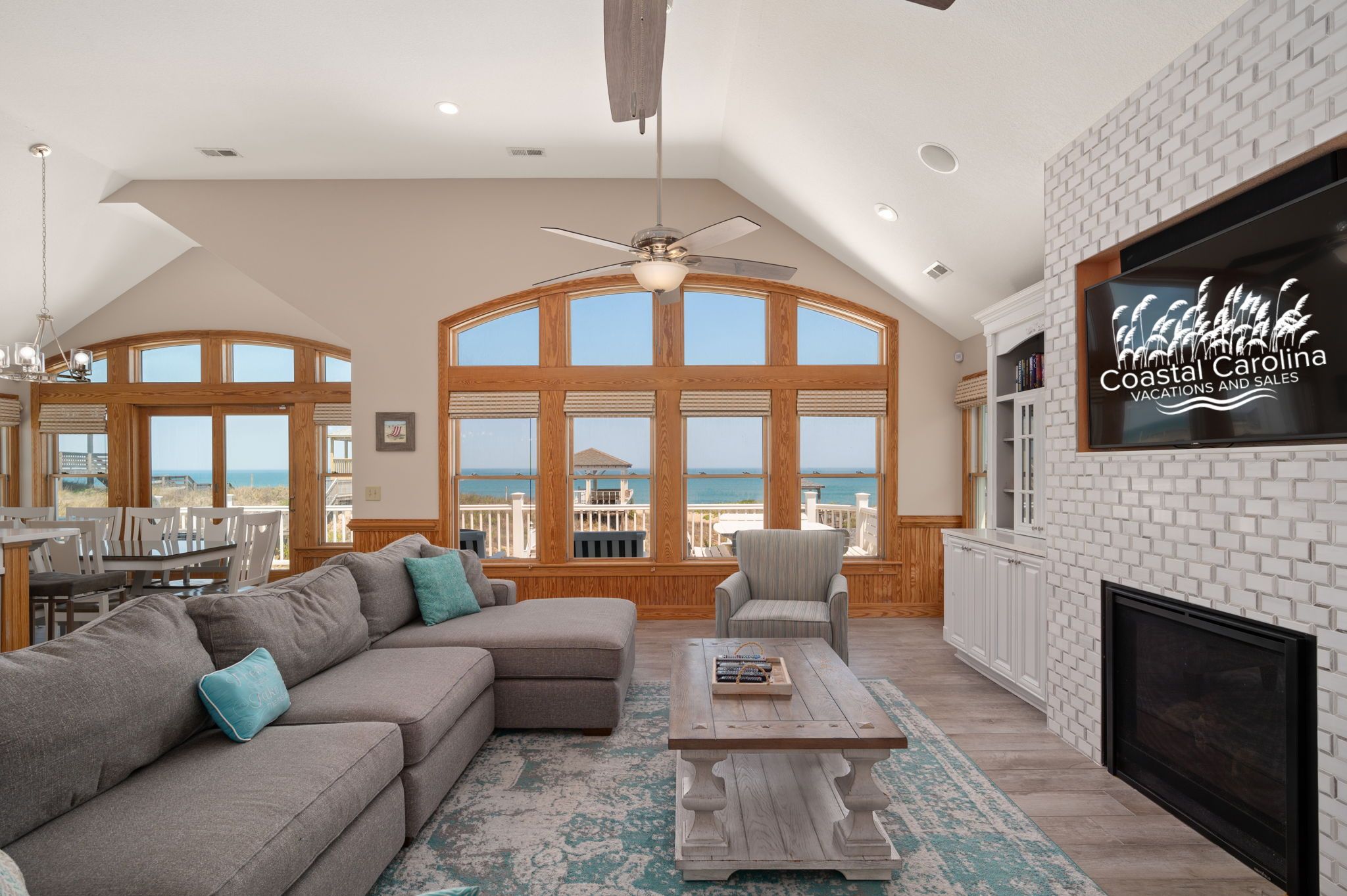 A spacious living room with a large window overlooking the ocean, a ceiling fan, and a fireplace.