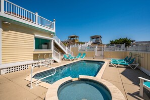 A swimming pool with a small hot tub, surrounded by lounge chairs and a wooden deck.