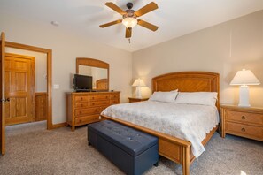 A bedroom with a wooden bed, a ceiling fan, a dresser, a television, and two bedside lamps. - Turtle's Nest: Oceanfront, pool, hot tub, theater & rec rooms and elevator! (Kill Devil Hills)