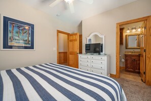 Une chambre à coucher comprenant un lit, une commode, un téléviseur et une salle de bain avec un miroir et un lavabo.