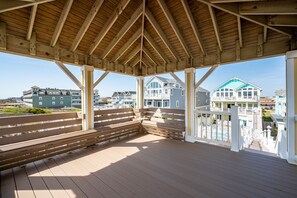 A wooden deck with benches, a covered area with a pitched roof, and a view of beachfront buildings. - Turtle's Nest: Oceanfront, pool, hot tub, theater & rec rooms and elevator! (Kill Devil Hills)