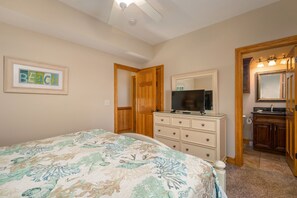 A bedroom with a bed, dresser, television, and a bathroom visible through an open door. - Turtle's Nest: Oceanfront, pool, hot tub, theater & rec rooms and elevator! (Kill Devil Hills)