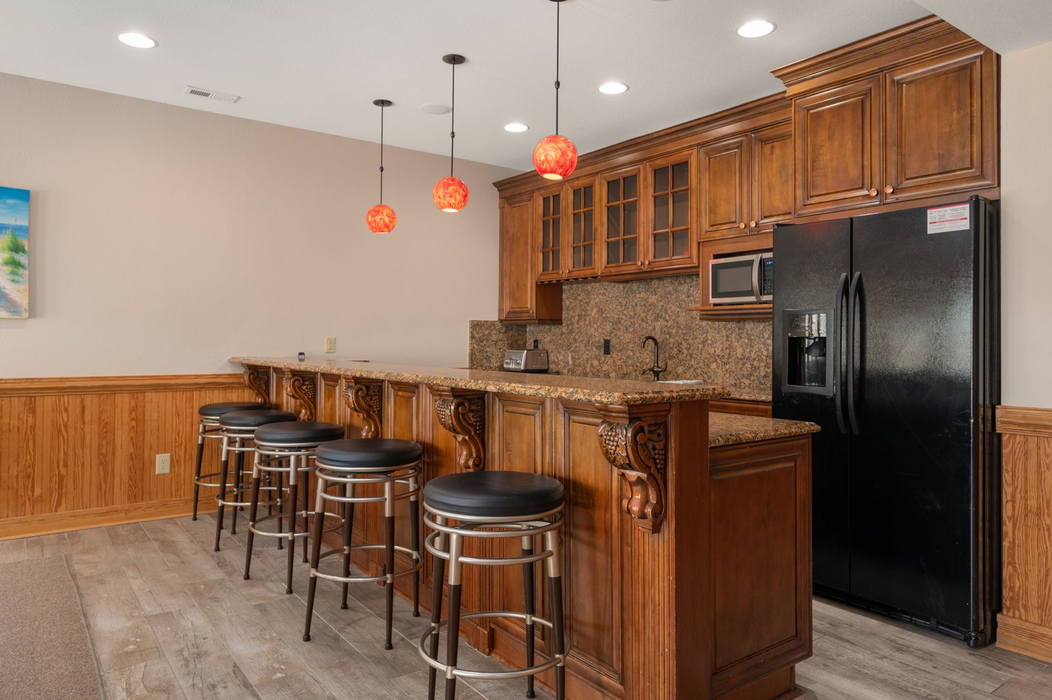 Una cocina con muebles de madera, un refrigerador negro, microondas y una barra con taburetes.
