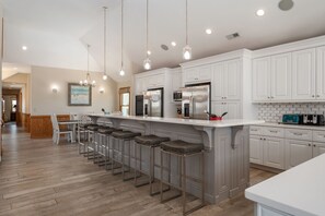 A modern kitchen with white cabinetry, stainless steel appliances, and a bar area with stools.
