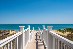 A wooden boardwalk leading to a beach with white railings.