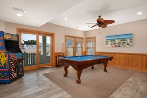 A pool table in a room with wooden flooring, a ceiling fan, and a view through a glass door.