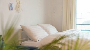 Ein ordentlich bezogenes Bett mit weißer Bettwäsche in einem Zimmer mit weißer Wand und einem Fenster mit Vorhängen.