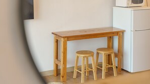 Eine kleine Küche mit einem Holztisch und zwei Barhocker, einem weißen Kühlschrank und einer Mikrowelle darauf.