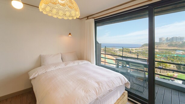 Ein Schlafzimmer mit einem großen Bett, einer Deckenleuchte und Blick auf einen Balkon mit Sitzgelegenheit.