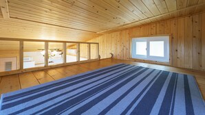 Ein geräumiger Raum mit Holzwänden und einem großen Fenster, mit einem blau gestreiften Teppich und einem sichtbaren Küchenbereich.
