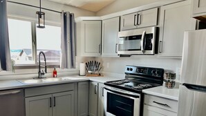 A modern kitchen with grey cabinets, a stainless steel stove, a microwave, and a refrigerator. - Luxury Stay w/Coffee Bar & Movie Room, 2 King Suites, Firepit — Black Hills View (Rapid City)