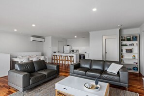 A modern living room with two leather sofas, a white coffee table, and a kitchen area in the background. - Panoramic Beach house, modern & immaculately presented to sleep up to 10 guests (Carrickalinga)