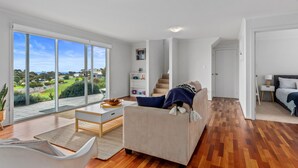 Un vaste espace de vie comprenant une grande porte-fenêtre coulissante donnant sur un balcon, un canapé, une table basse et un escalier menant à une autre pièce.